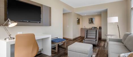 A modern living room with a flat-screen TV, a desk, a chair, a sofa, and a dining area.