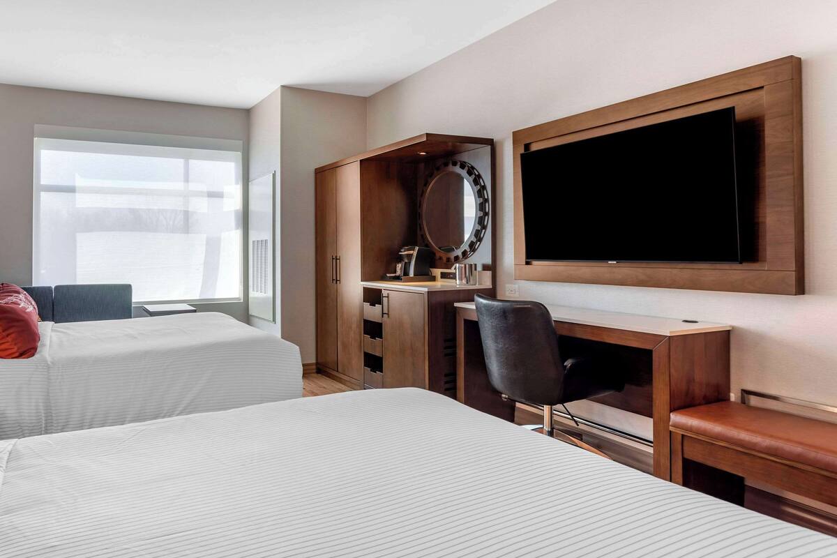Une chambre d’hôtel avec deux lits, un bureau avec un miroir, une télévision et une fenêtre donnant sur le paysage.