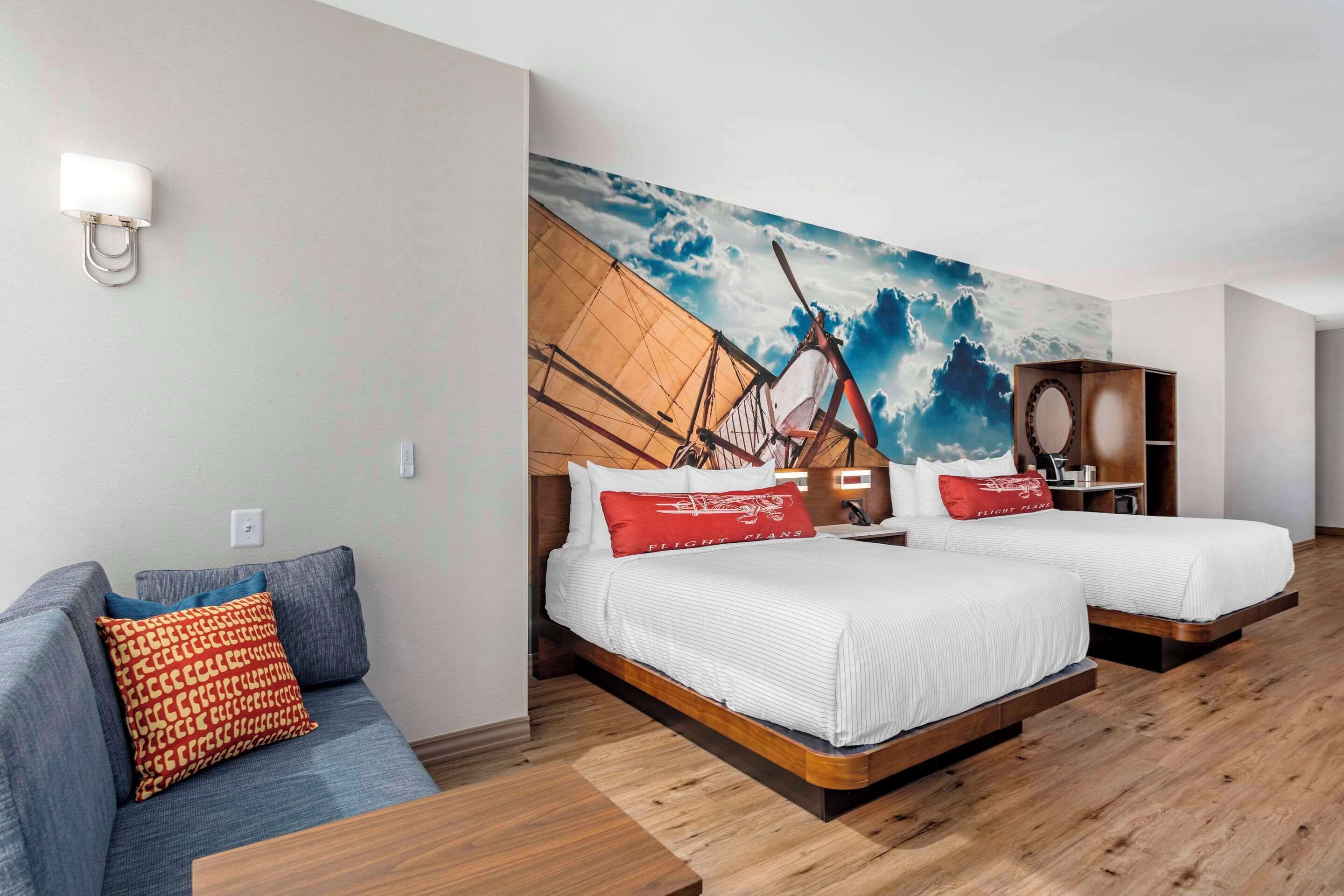 Una habitación de hotel con dos camas, un sofá y un mural de un velero en la pared.