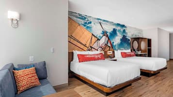 Una habitación de hotel con dos camas, un sofá y un mural de un velero en la pared.