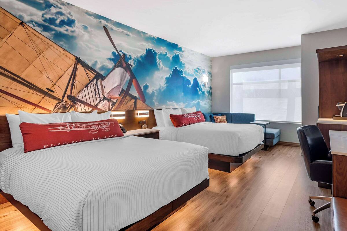 Une chambre d’hôtel avec deux lits, un bureau et une grande fresque représentant un navire sur le mur.