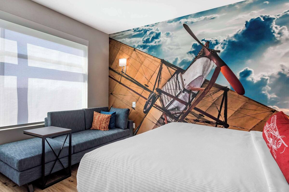 Une chambre d’hôtel avec un lit, un canapé, une petite table et une grande fresque représentant un voilier sur le mur.