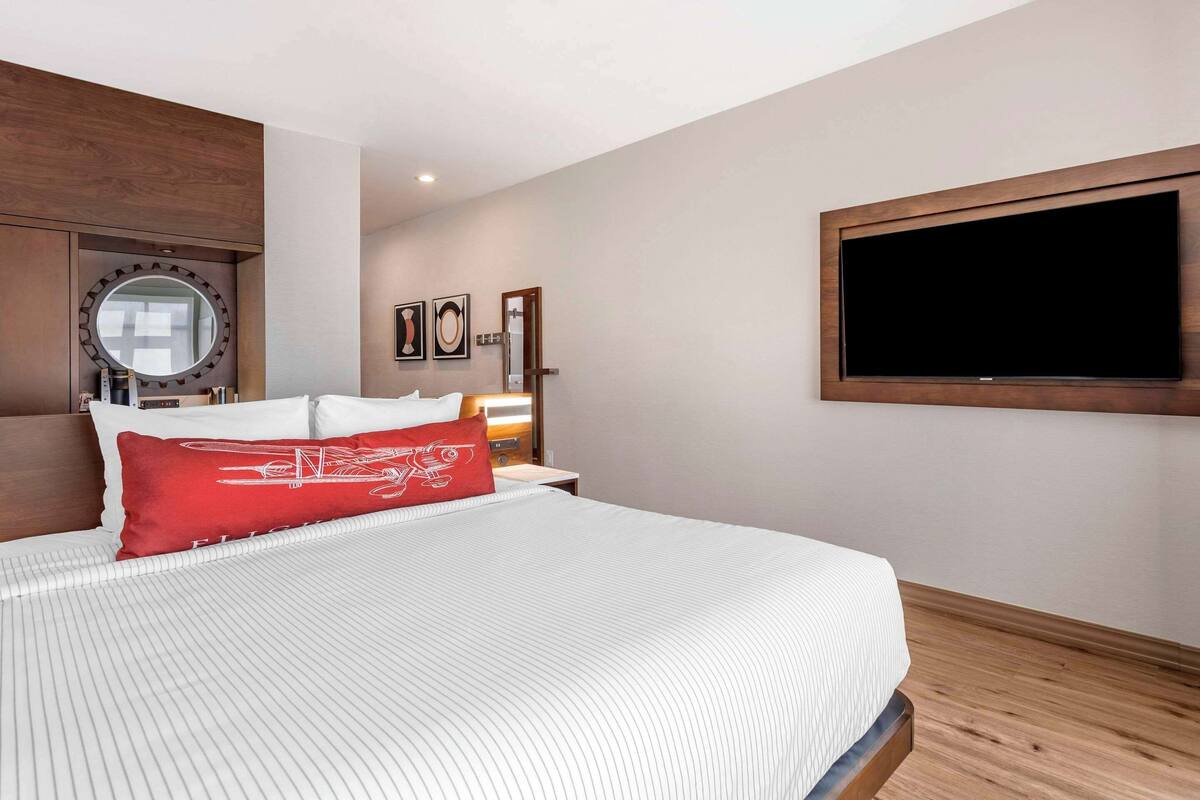 Une chambre d’hôtel avec un grand lit, un téléviseur fixé au mur, une tête de lit en bois et un miroir.
