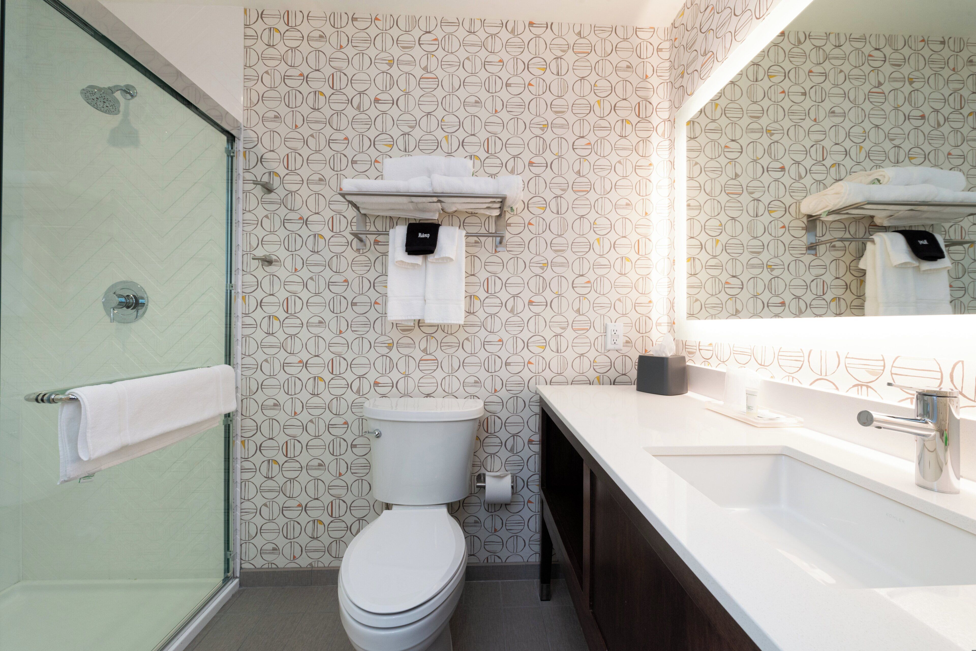 Un baño moderno con inodoro, lavamanos, espejo y ducha.