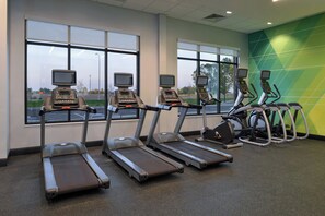 A gym with treadmills and stationary bikes, large windows, and a green wall.