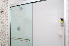 Ducha con mampara de vidrio, barra de apoyo, cabezal de ducha y dispensador de jabón en la pared.