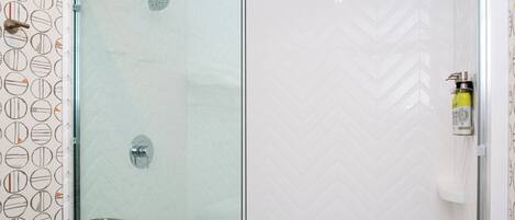 Ducha con cerramiento de vidrio, grifo de cromo y toallero en la pared.