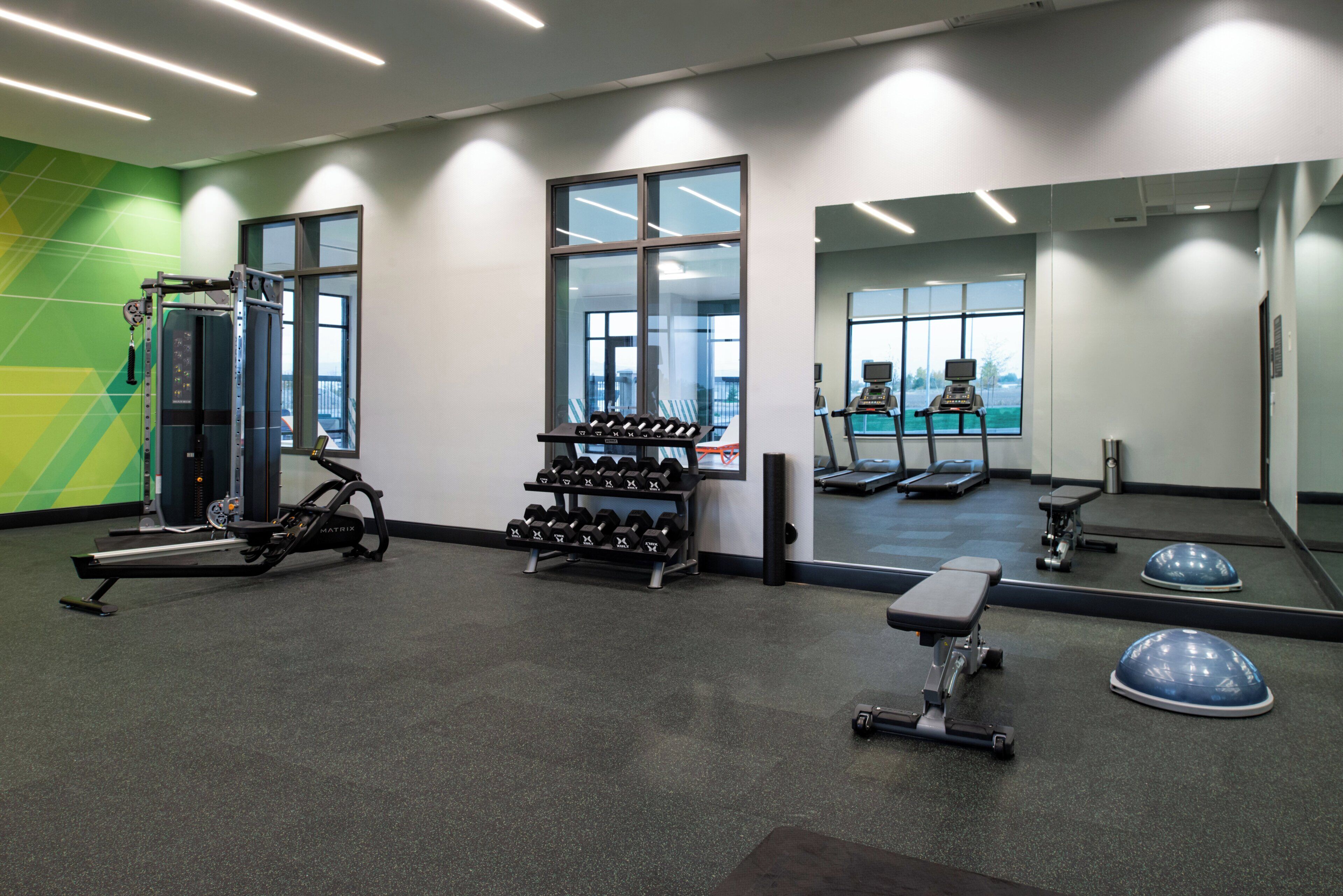 A gym with cardio equipment, weight benches, and dumbbells.