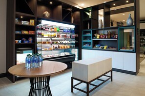 A modern retail space with shelves stocked with various products, a refrigerated display case, and a seating area with a table and bench.