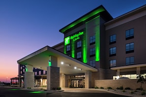 Um hotel Holiday Inn com fachada moderna, várias entradas e área de estacionamento coberta.