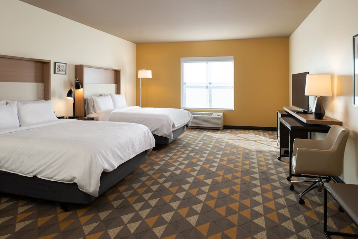 Une chambre d’hôtel avec deux lits, un bureau, une chaise et une grande fenêtre.