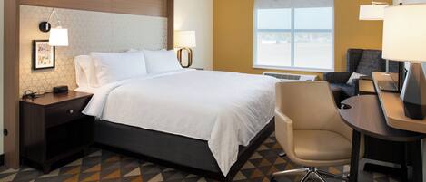 A hotel room with a bed, bedside tables, a desk, a chair, and a window.