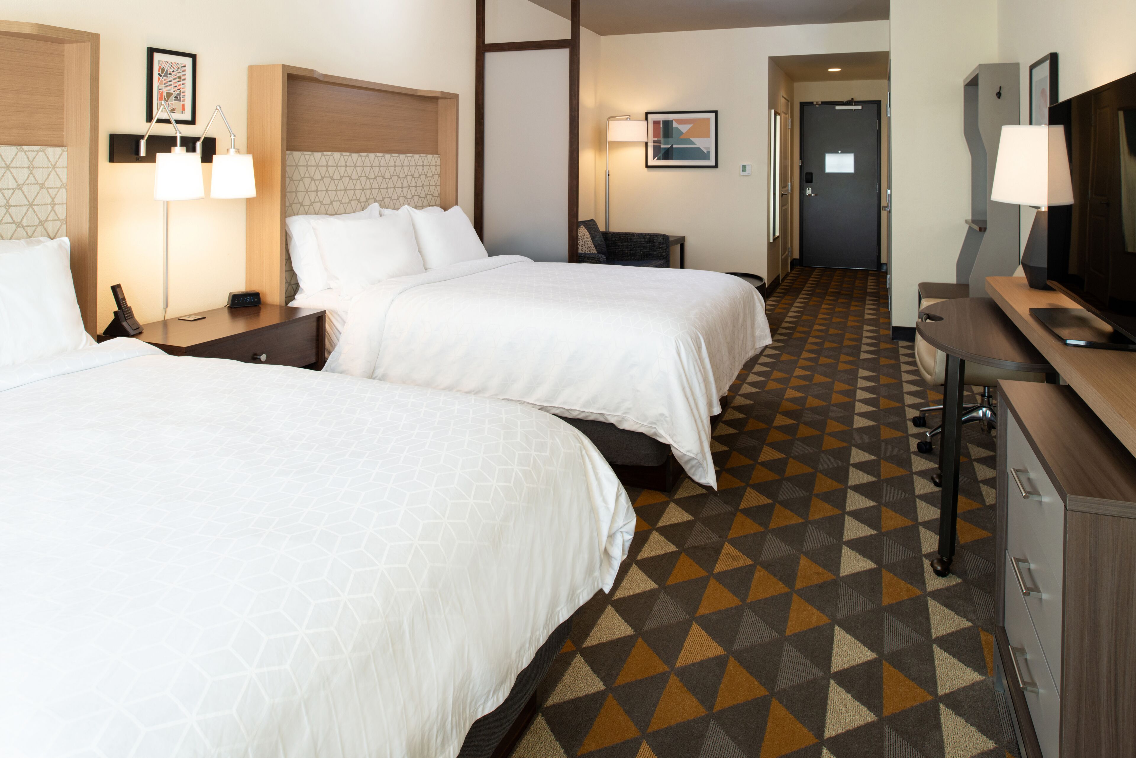 Une chambre d’hôtel avec deux lits, un bureau, une chaise, un téléviseur et un sol à motifs.