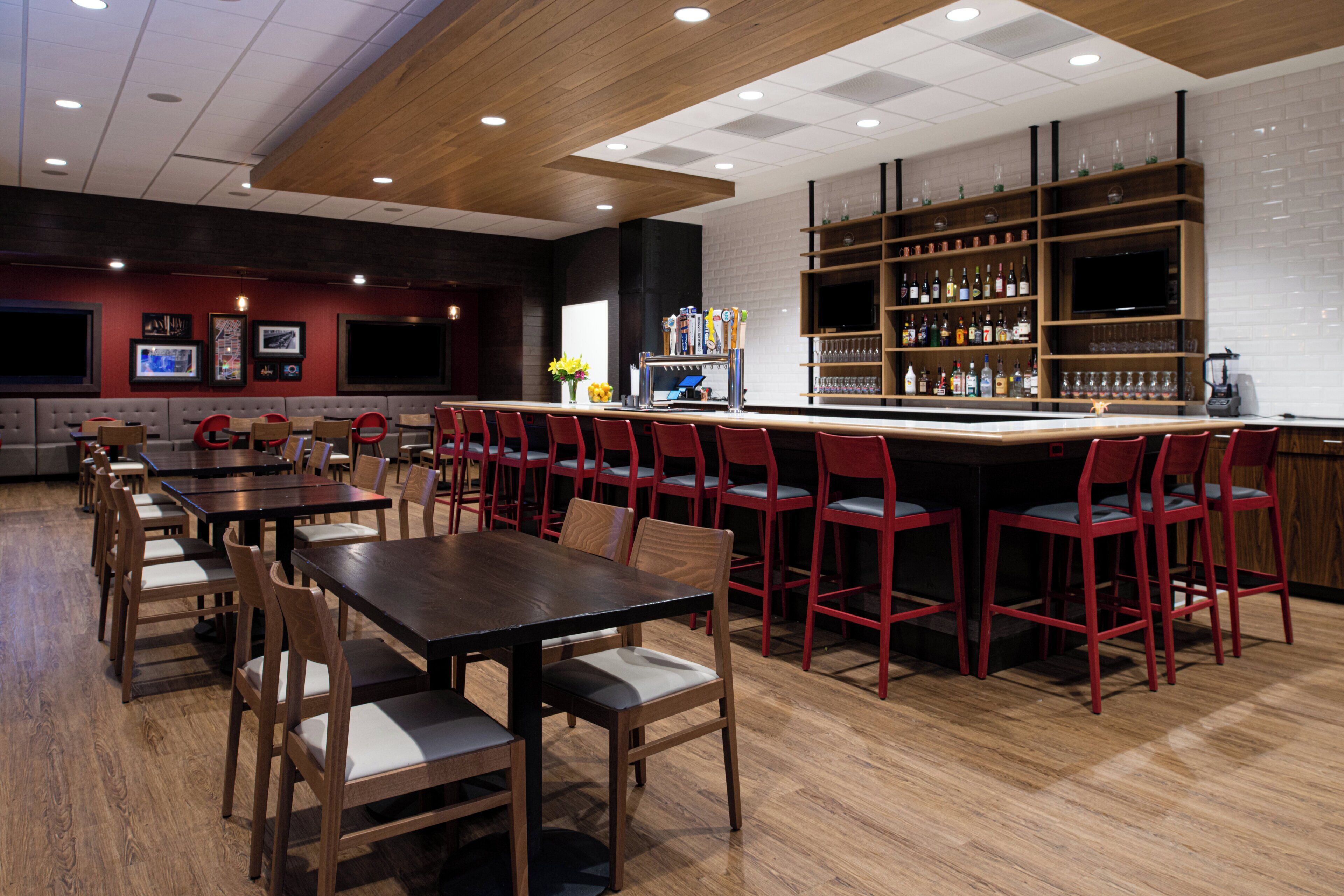 Een restaurant met houten tafels en stoelen, een bar met flessenplanken, en een televisiescherm.