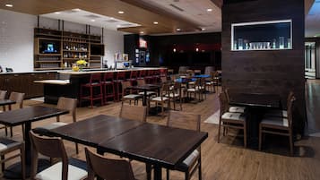 Een restaurant met meerdere tafels en stoelen, een bar met flessenrekken en een wandvitrine.