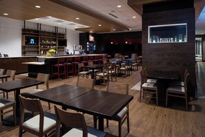 Un restaurant doté de nombreuses tables et chaises, d’un bar avec des étagères remplies de bouteilles et d’une vitrine murale.