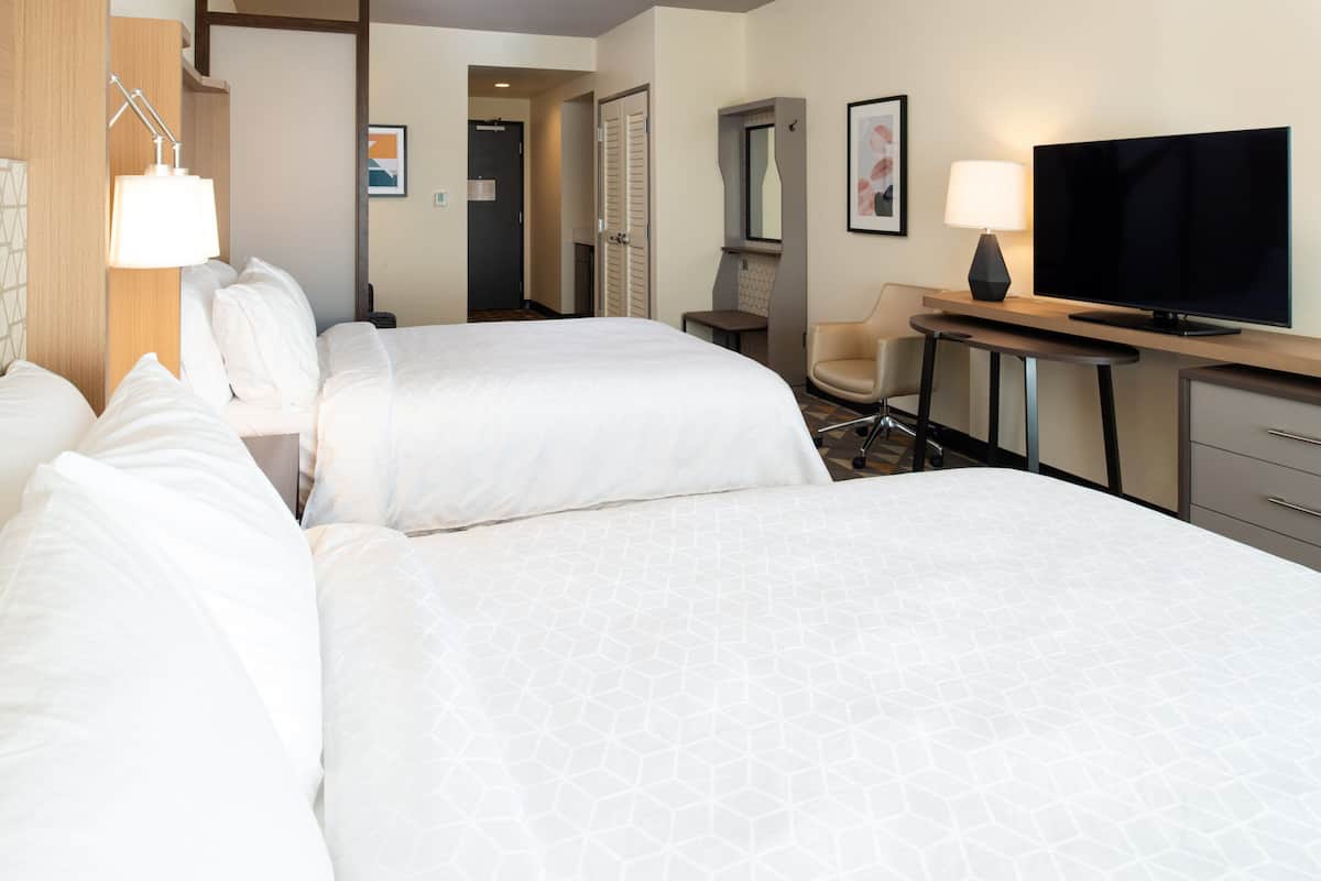 Une chambre d’hôtel avec deux lits, un bureau équipé d’une télévision, une chaise et une lampe.