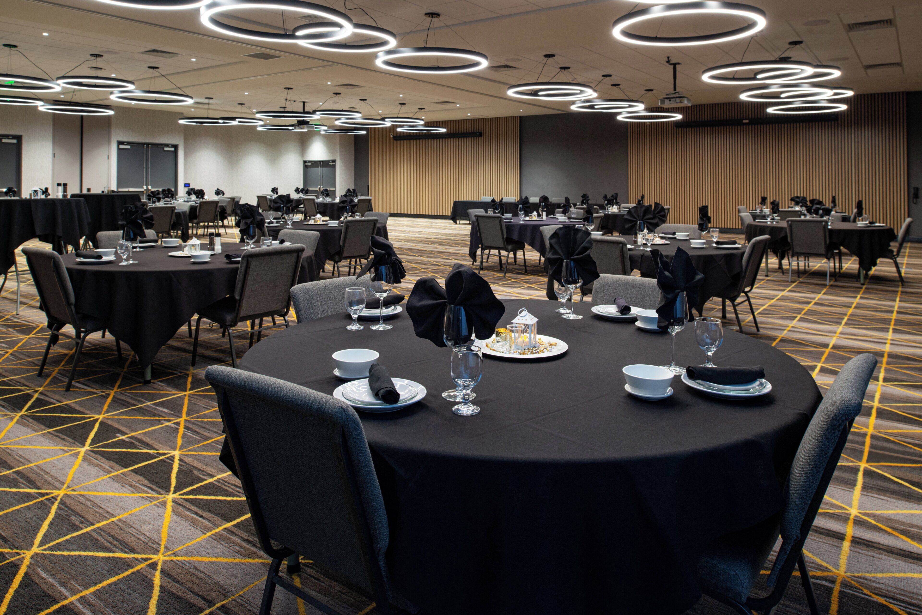 A banquet hall with round tables, chairs, and a carpeted floor.