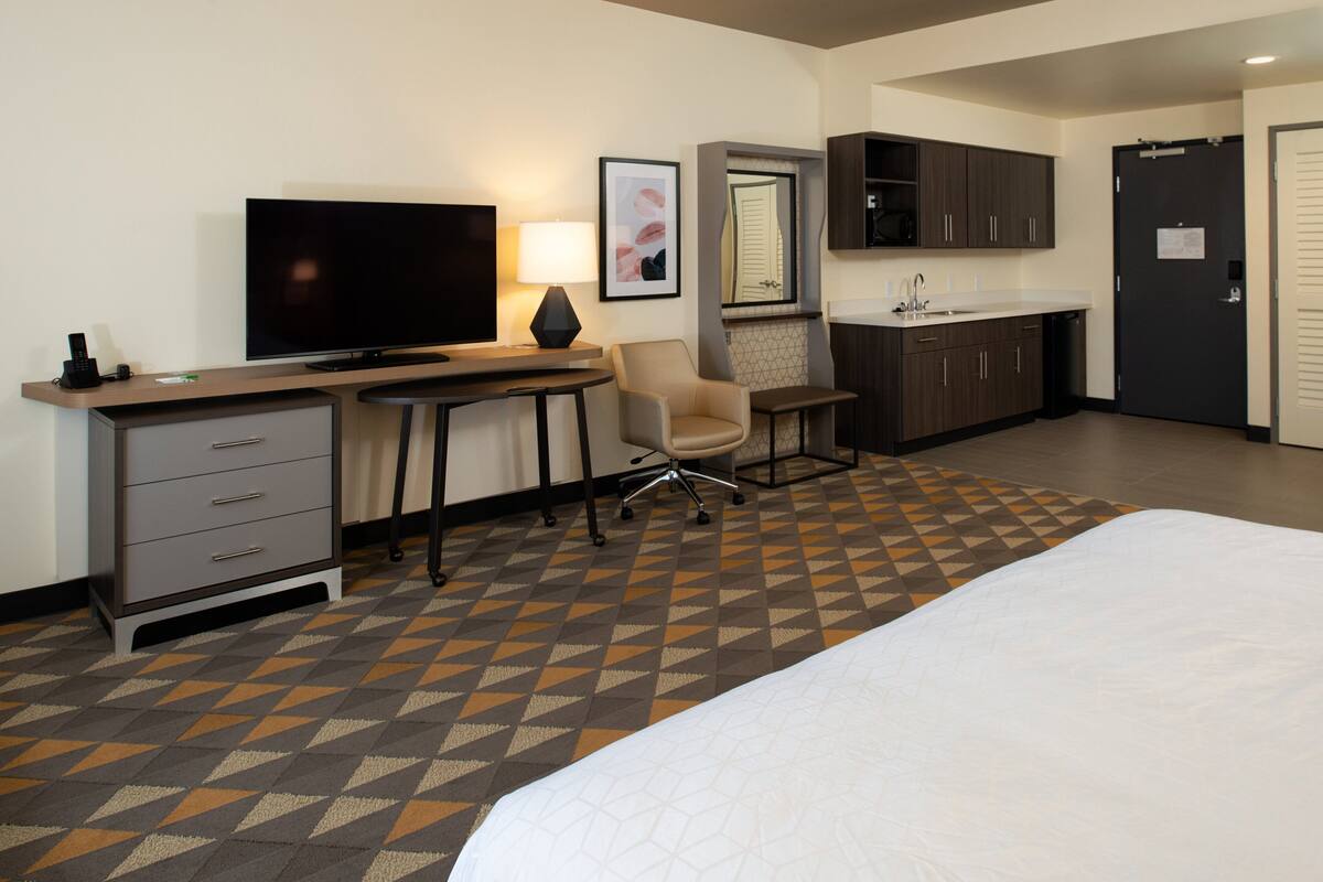 Une chambre d’hôtel comprenant un lit, un bureau avec une télévision, une chaise, un coin cuisine et une salle de bain.