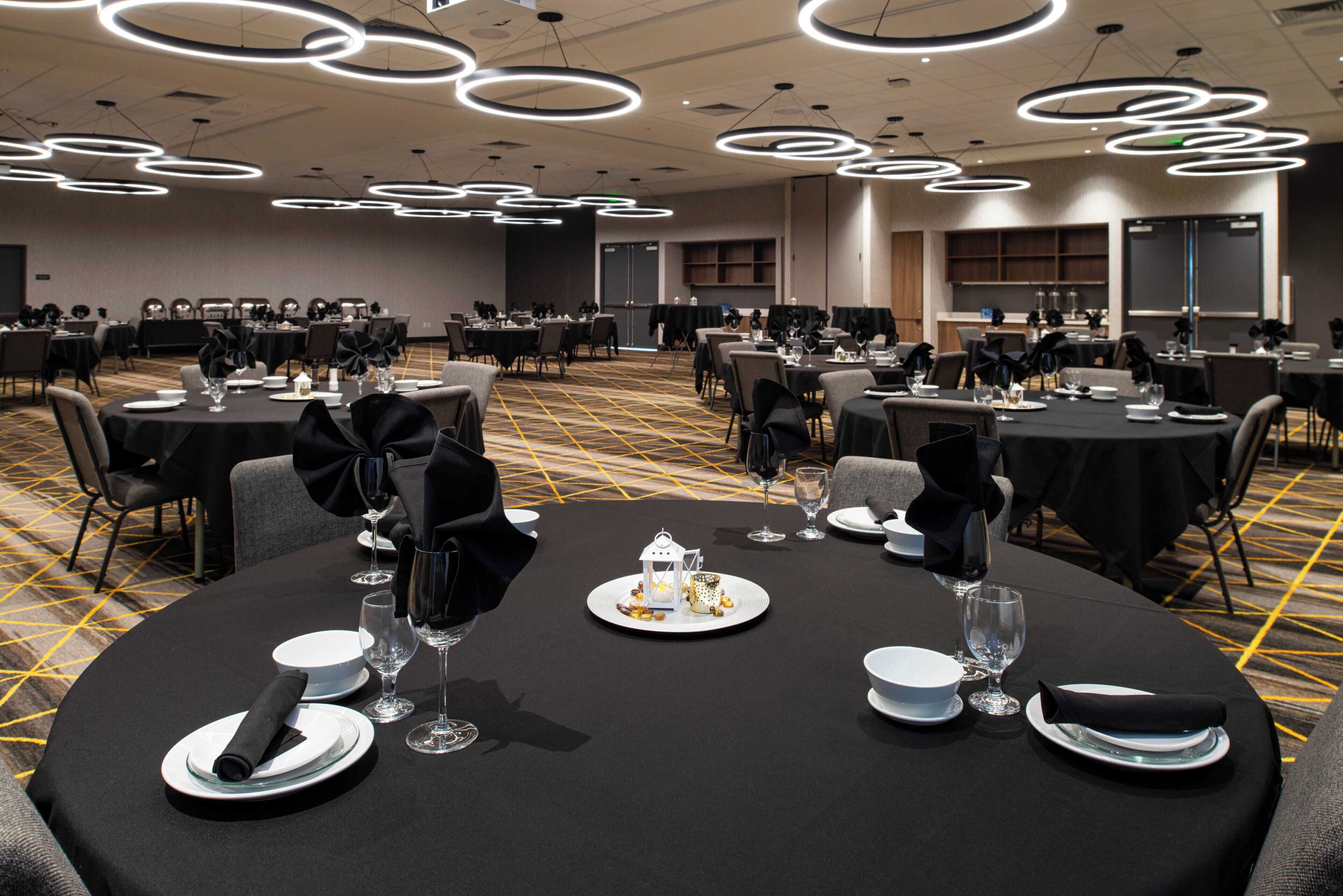 A banquet hall with round tables set for dining, featuring black tablecloths and white plates.