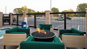 Een terras met rieten meubels en een vuurkuil in het midden.