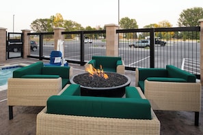 An outdoor seating area with wicker furniture and a central fire pit.