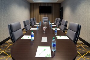 A conference room with a long table, chairs, water bottles, and a flat-screen TV on the wall.