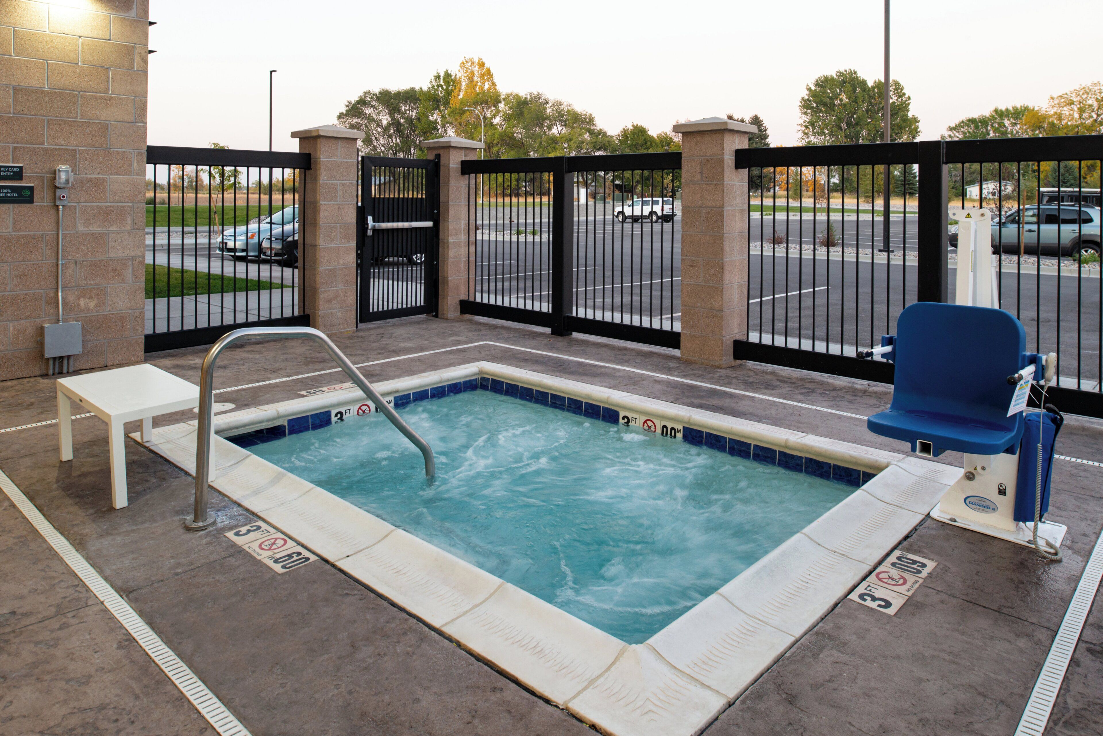 A hot tub with a safety rail, a bench, and a pool area with a fence.
