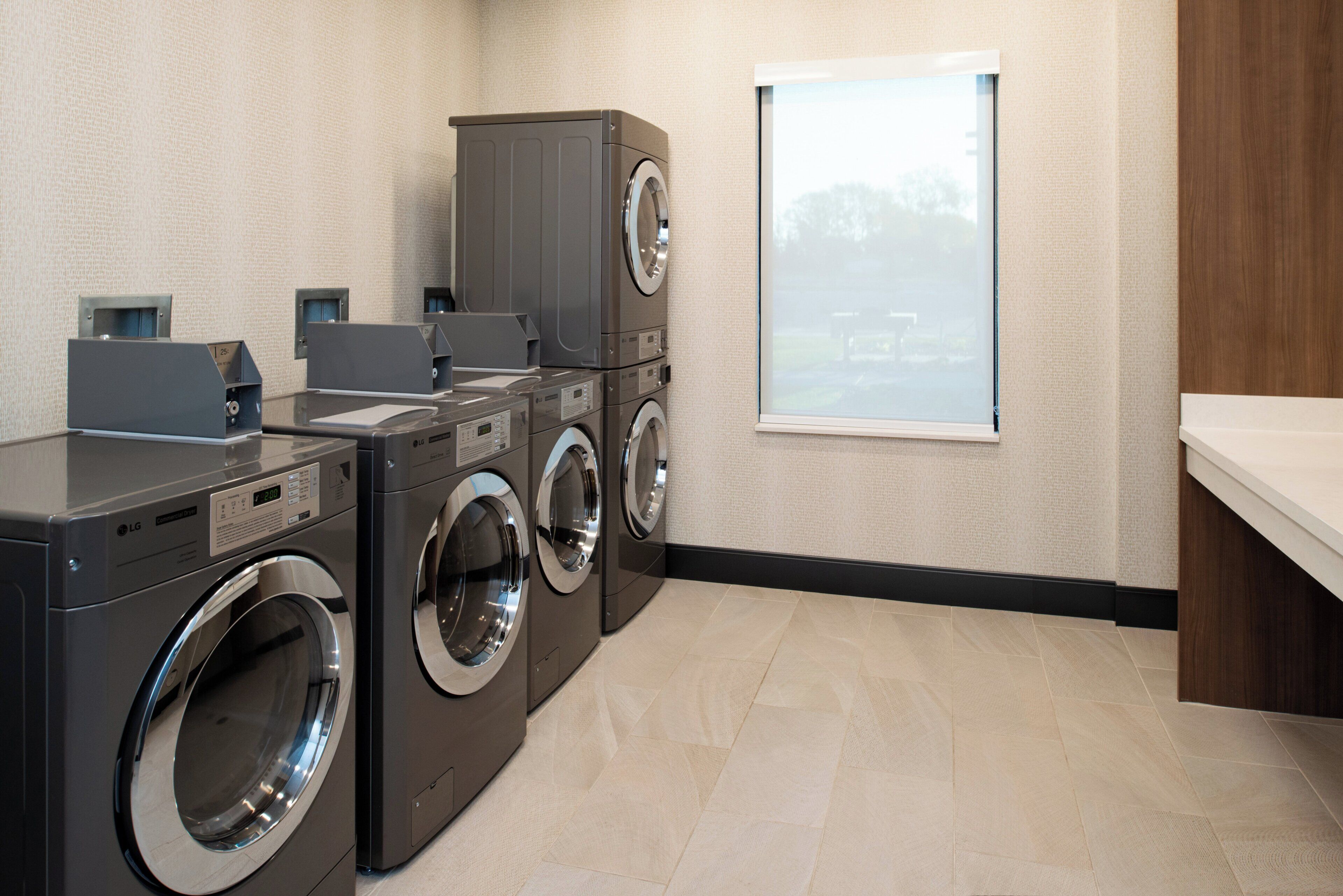 A laundry room with stacked washers and dryers, a window with a view, and a tiled floor.