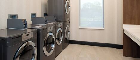 A laundry room with stacked washers and dryers, a window with a view, and a tiled floor.