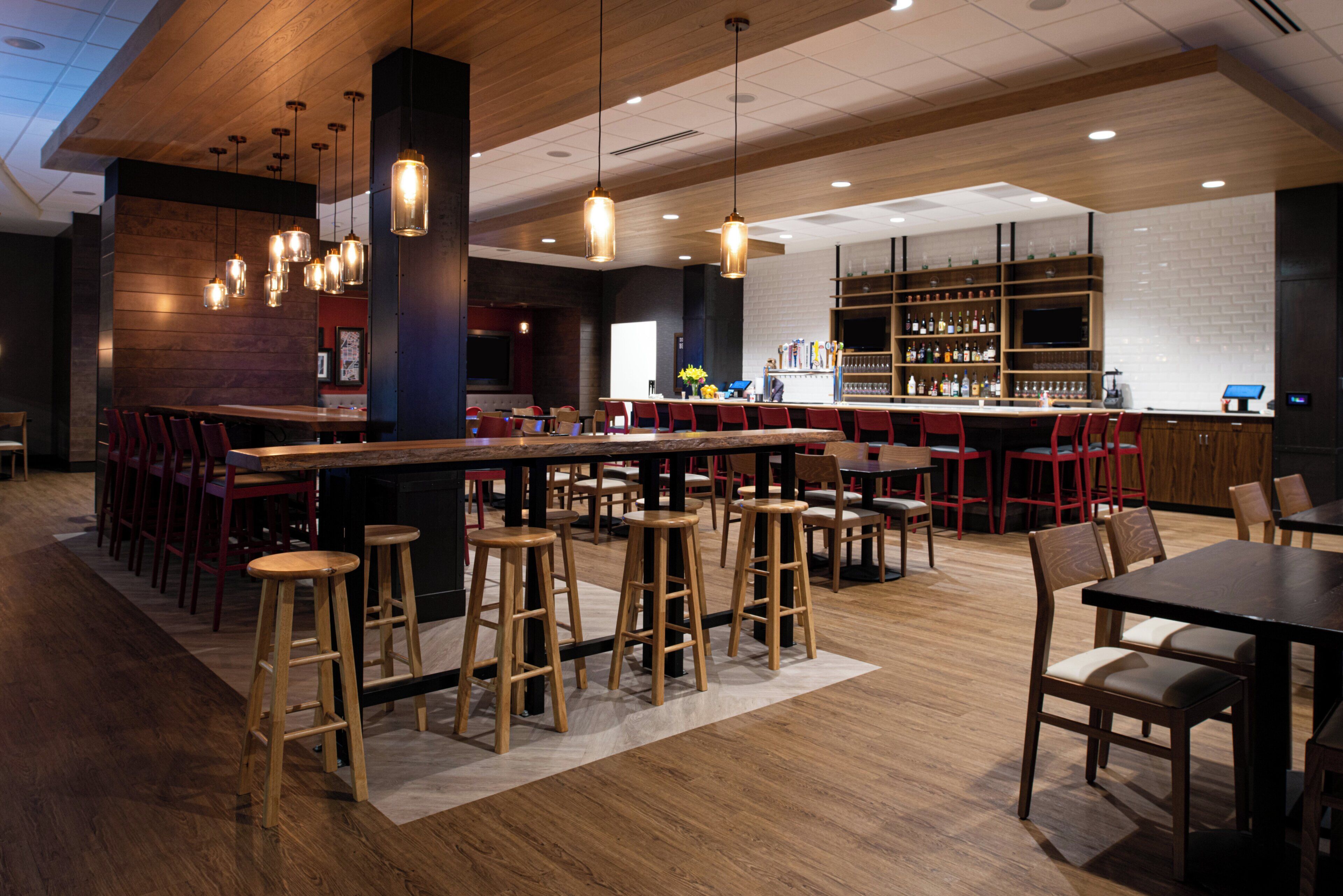 Een moderne bar met houten krukken, een lange bar en een toonbank vol flessen.