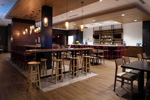 Een moderne bar met houten krukken, een lange bar en een toonbank vol flessen.