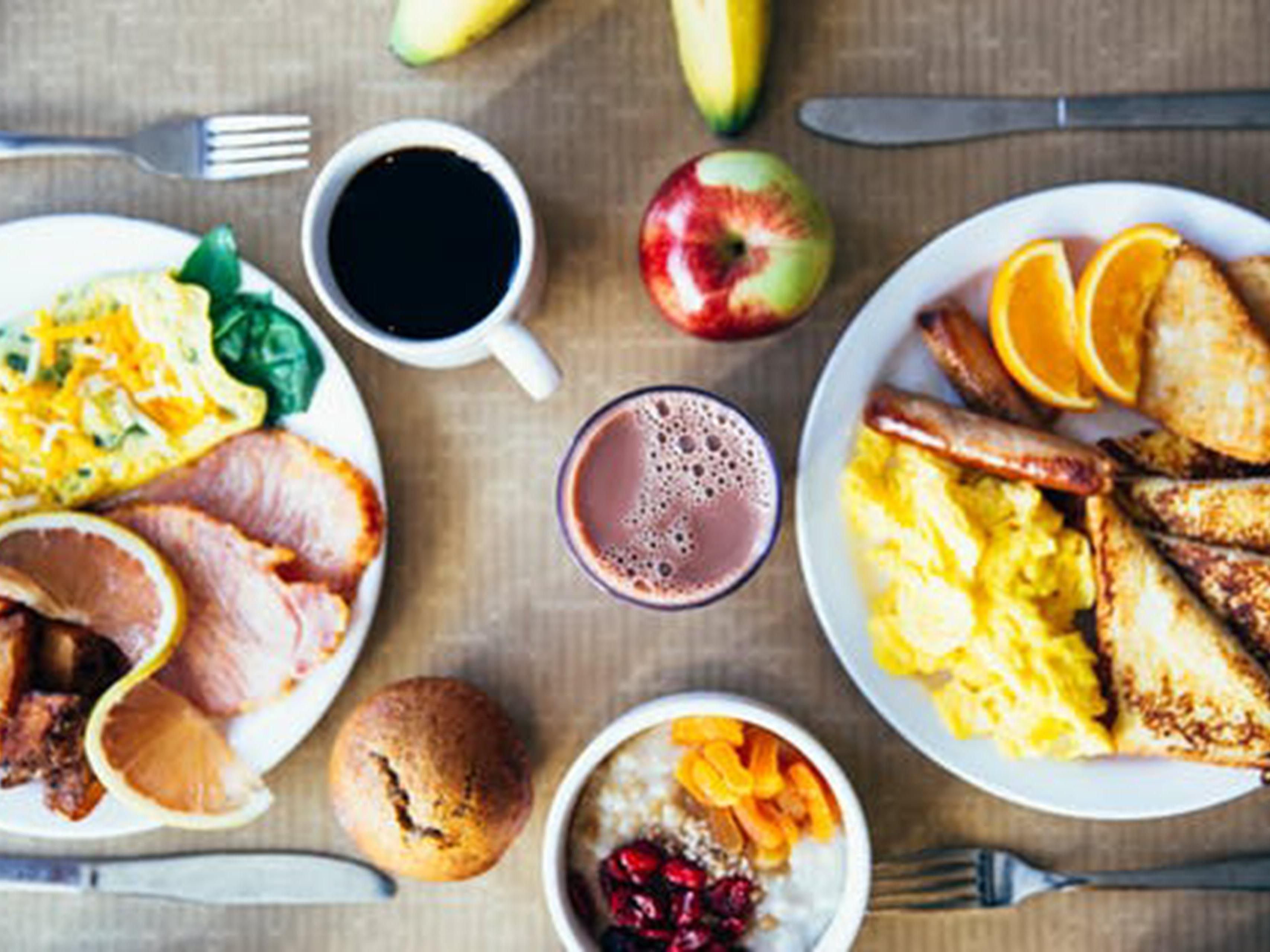 Une table de petit-déjeuner avec divers plats, notamment des œufs brouillés, des toasts, du bacon et des fruits.