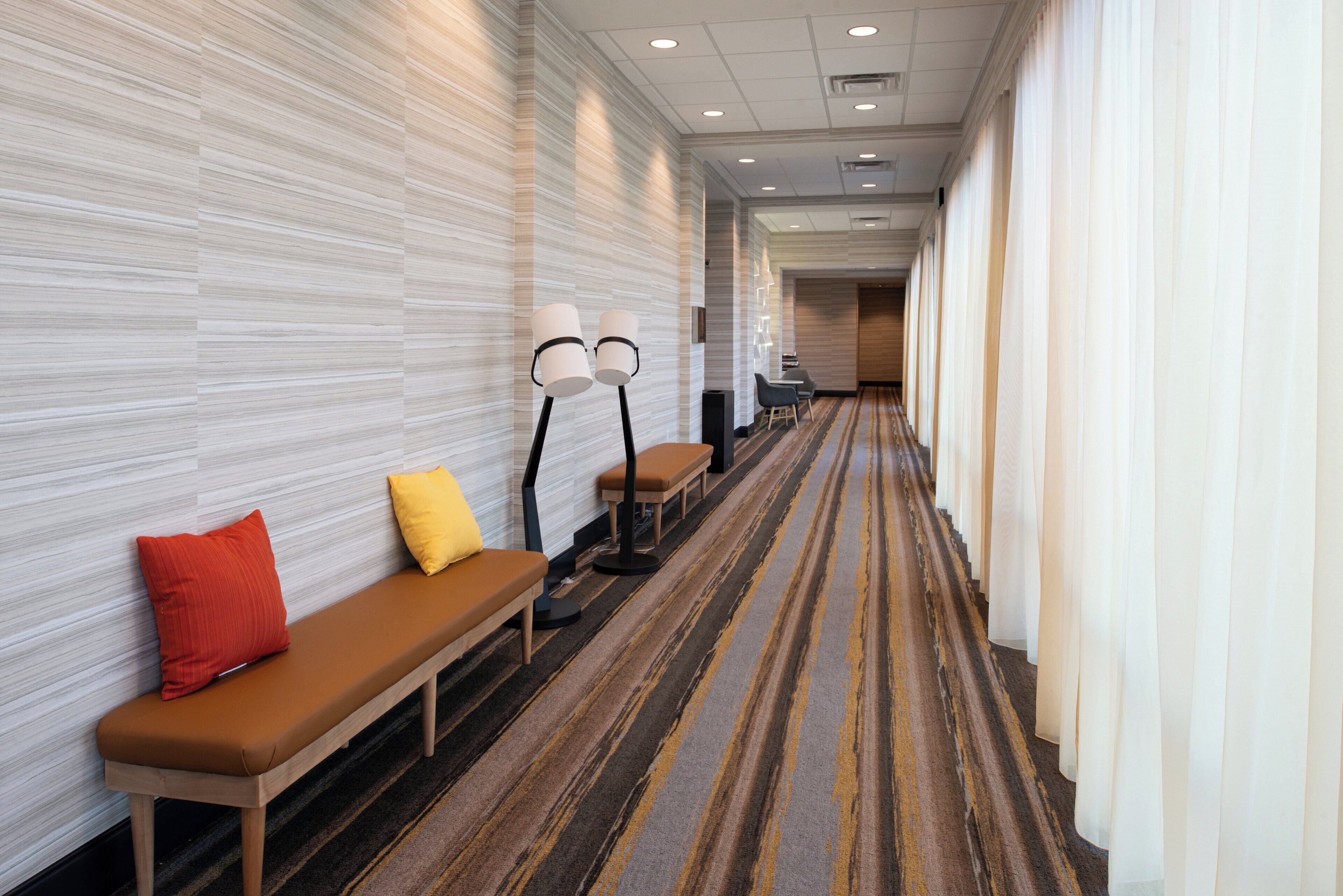 A hotel corridor with benches, lamps, and a patterned carpet.