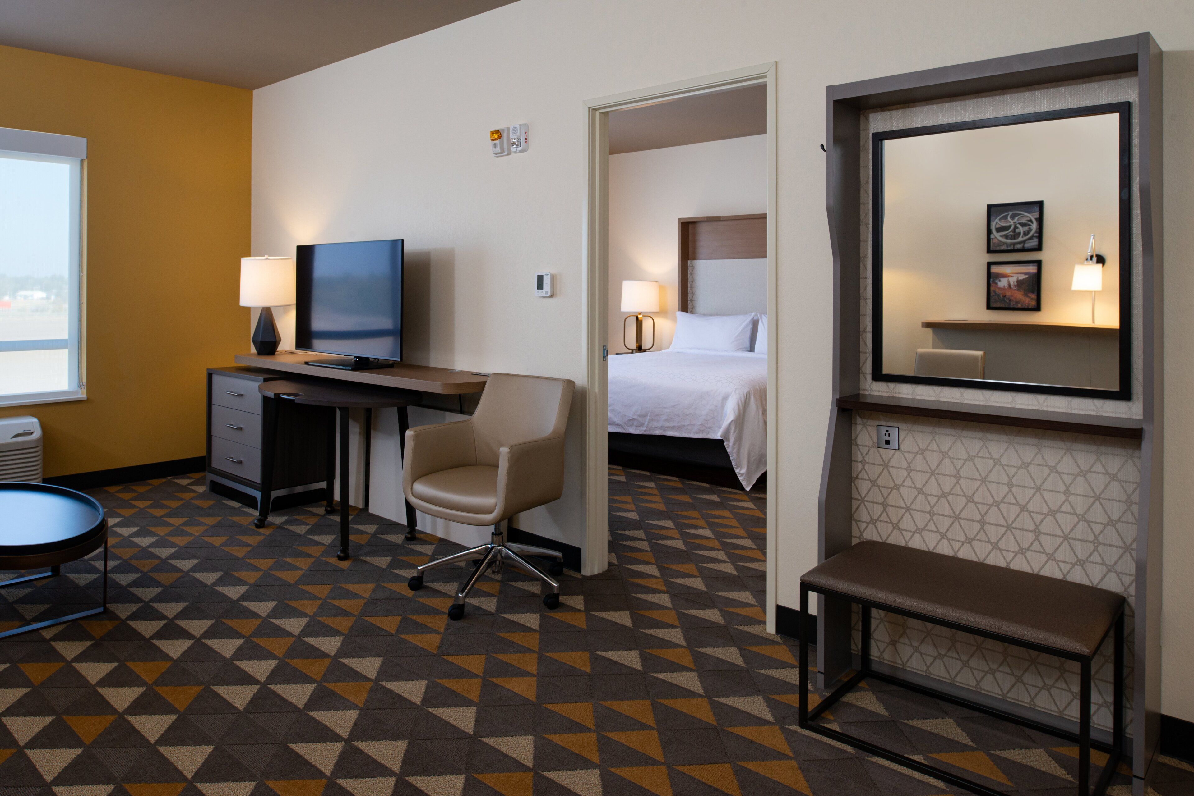 Habitación de hotel con escritorio, silla, cama y un espejo grande.