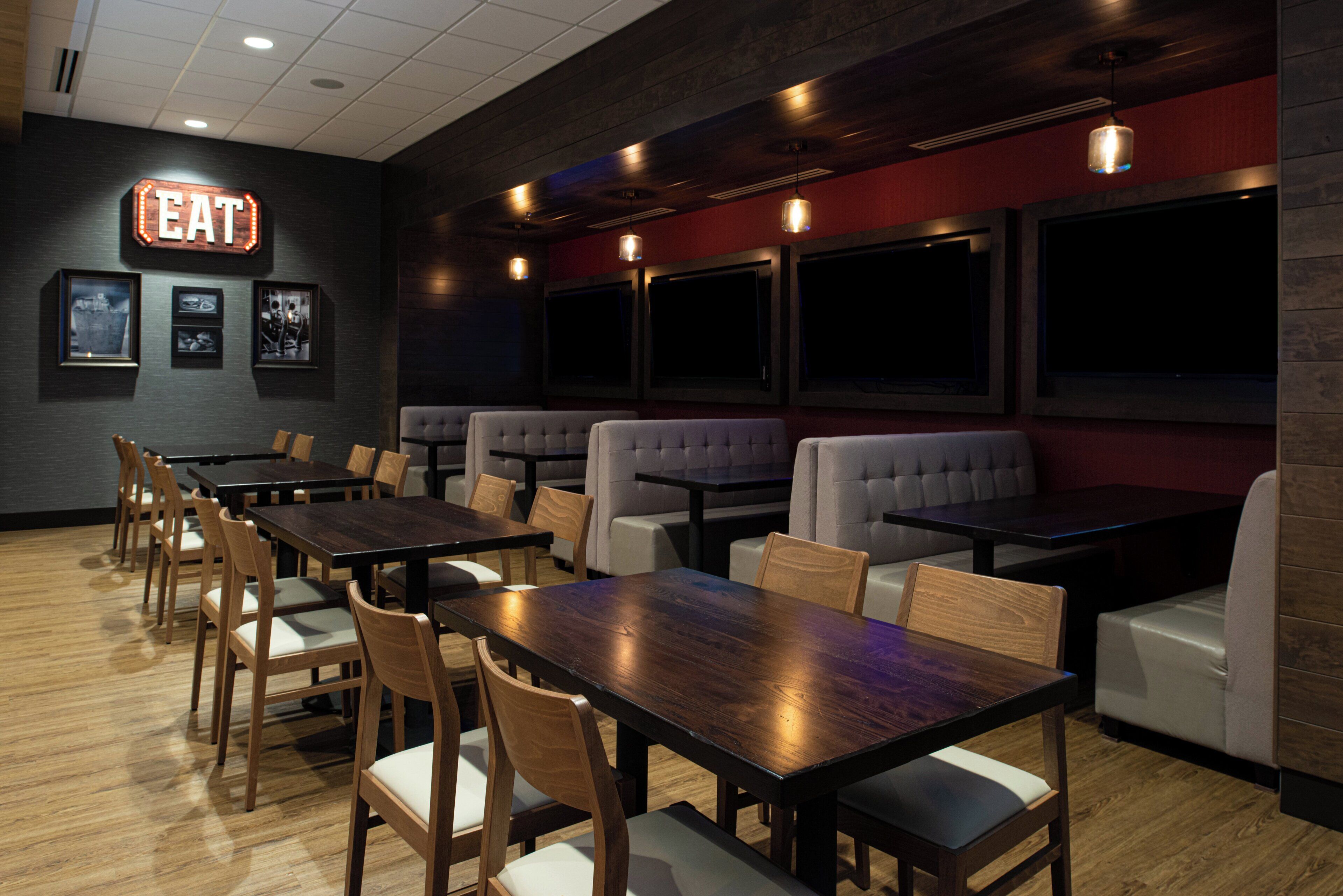 A restaurant with wooden tables and chairs, a neon 'EAT' sign, and framed pictures on the wall.