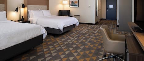 Habitación de hotel con dos camas, un escritorio, una silla, un televisor y una alfombra estampada.