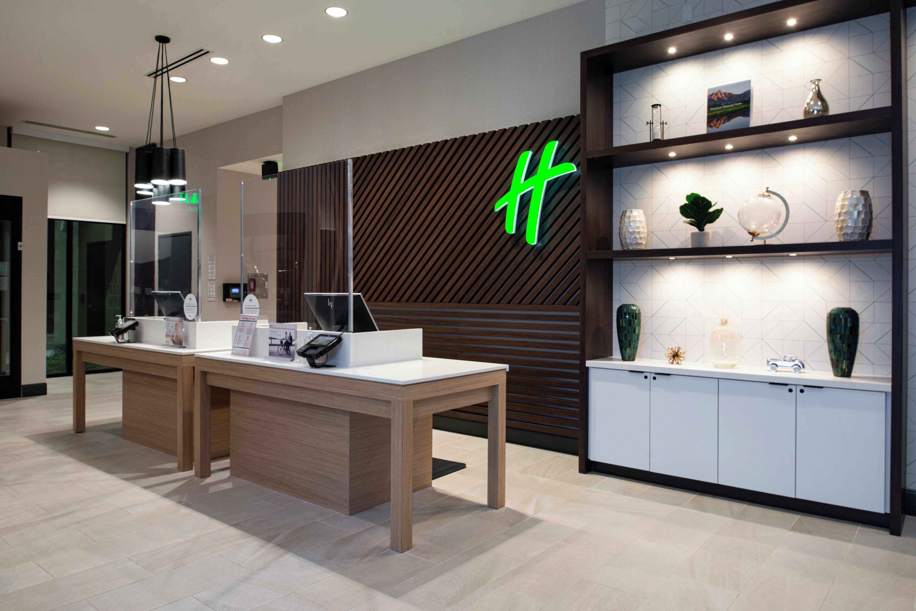 A modern hotel reception desk with a digital display, a wooden counter, and a neon sign.