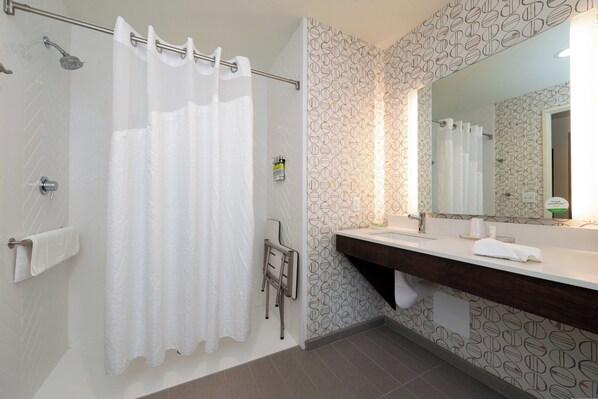 A bathroom with a shower, a towel rack, a sink with a mirror, and patterned wallpaper. - Holiday Inn & Suites Idaho Falls by IHG (Idaho Falls)