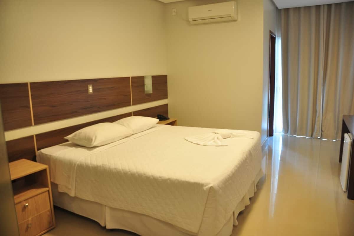 Habitación de hotel con una cama grande, cabecero de madera, una mesita de noche, un armario y un baño con ducha e inodoro.
