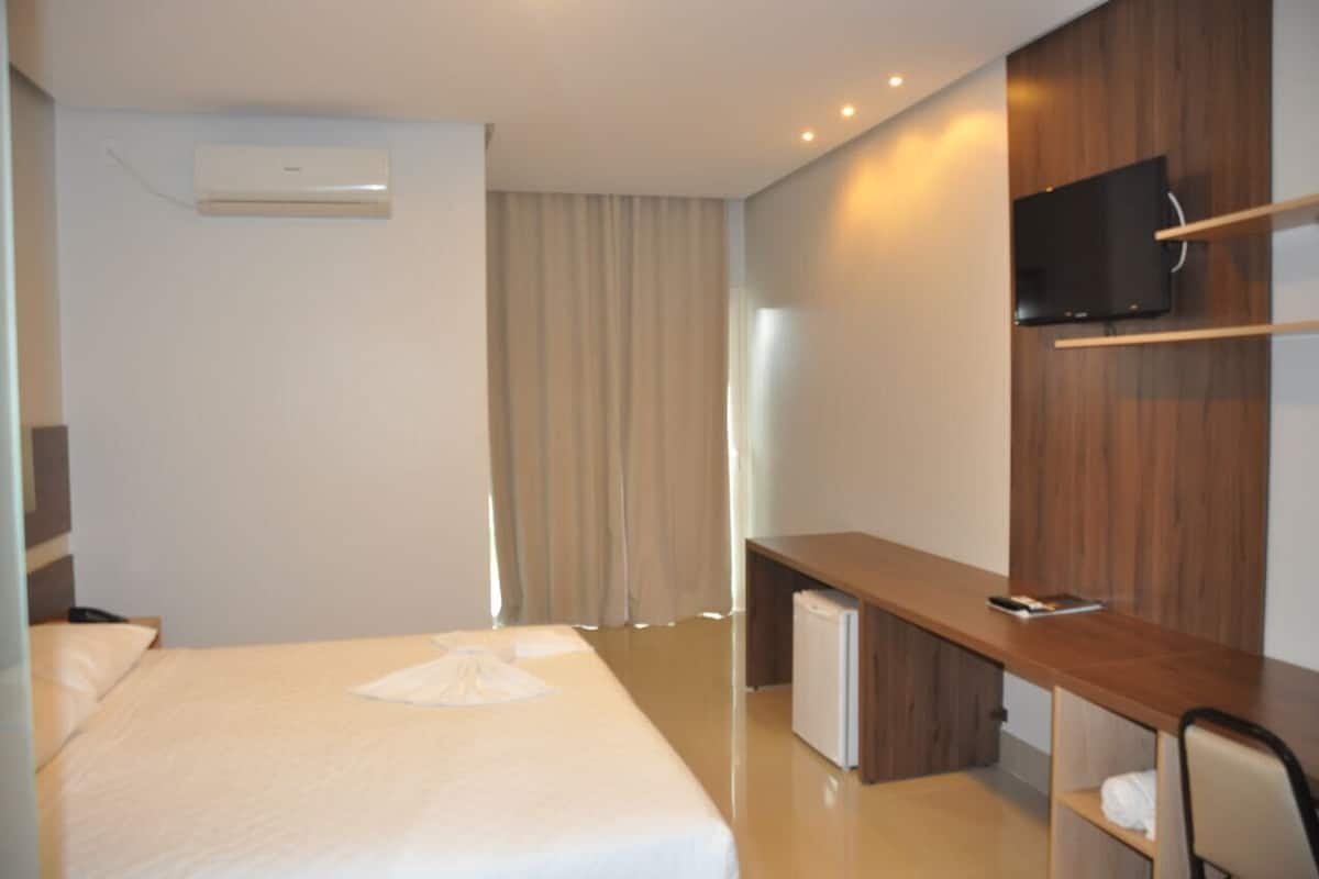 Una habitación de hotel con cama, escritorio, televisión y aire acondicionado.