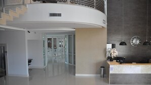 En moderne hotellobby med reception, trappe op til et højere plan, og et stort vægur.