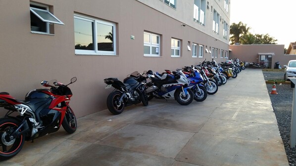 A row of motorcycles parked outside a building with multiple windows and a concrete floor.