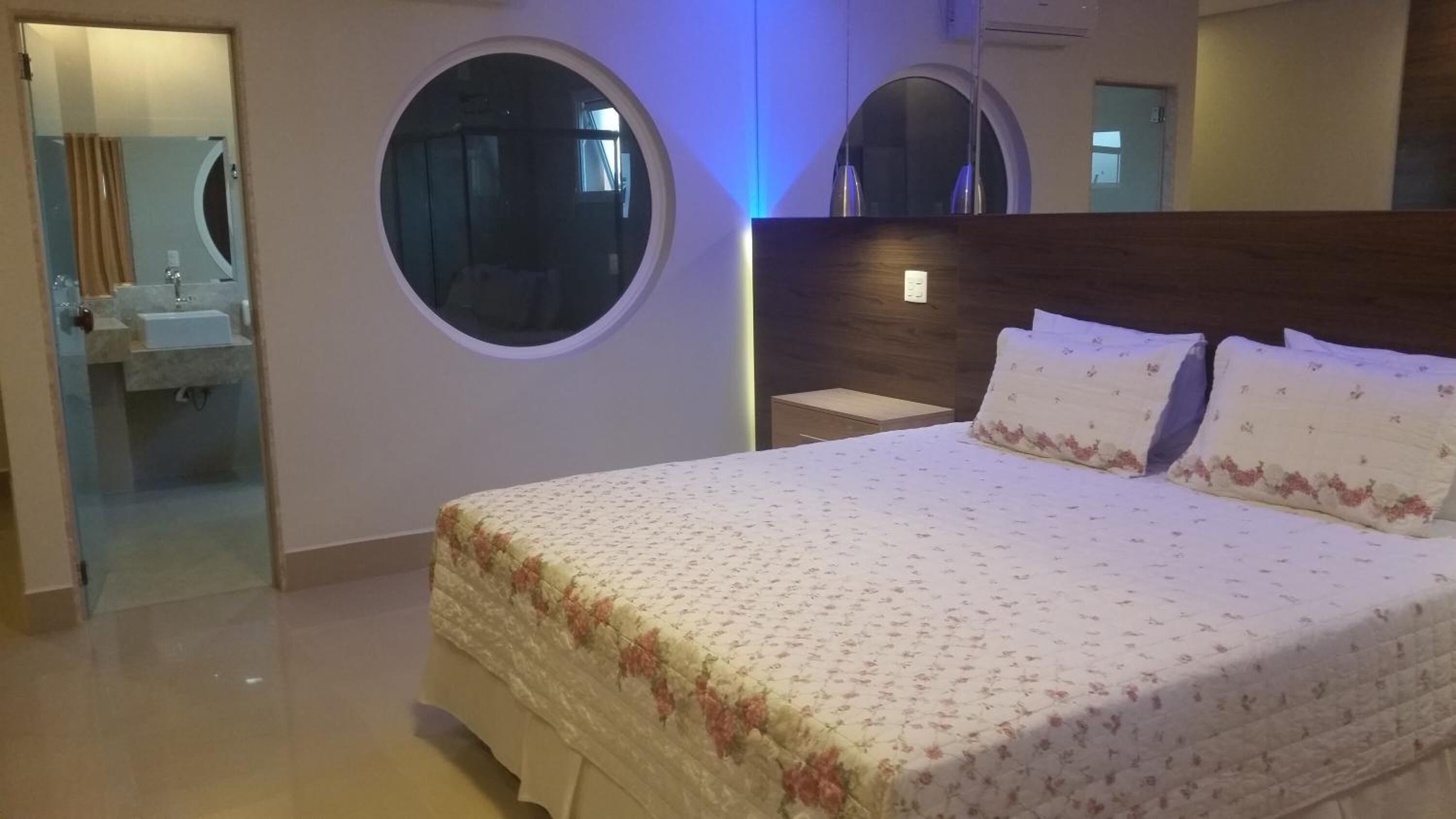 Un dormitorio con una cama grande, dos espejos redondos, un cabecero de madera y un baño visible a través de una puerta de cristal.