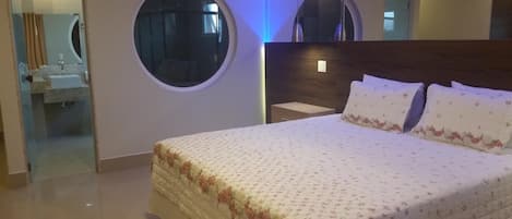 Un dormitorio con una cama grande, dos espejos redondos, un cabecero de madera y un baño visible a través de una puerta de cristal.