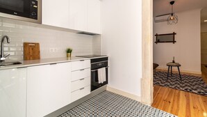 Una cocina moderna con armarios blancos, un microondas de acero inoxidable, un lavabo y una pequeña planta.