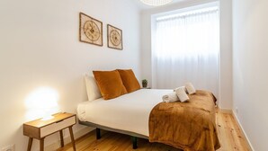 Un dormitorio con una cama, una mesita de noche, una lámpara y dos cuadros en la pared.