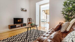 Un salón con sofá de cuero, televisor sobre un mueble de madera, alfombra estampada y una planta en maceta.