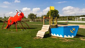Un parque infantil con una estructura de juego con forma de cangrejo rojo y una zona de juegos con forma de barco azul.