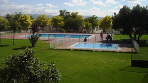 Un área de piscina con varias piscinas, rodeada de césped verde y árboles.